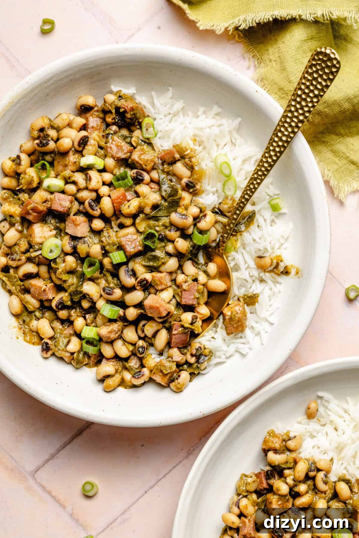 Classic Hoppin' John: Southern Black-Eyed Peas Recipe 2 Two completed dishes of Hoppin' Johns, served over white rice in white bowls. A green napkin is also on the counter.