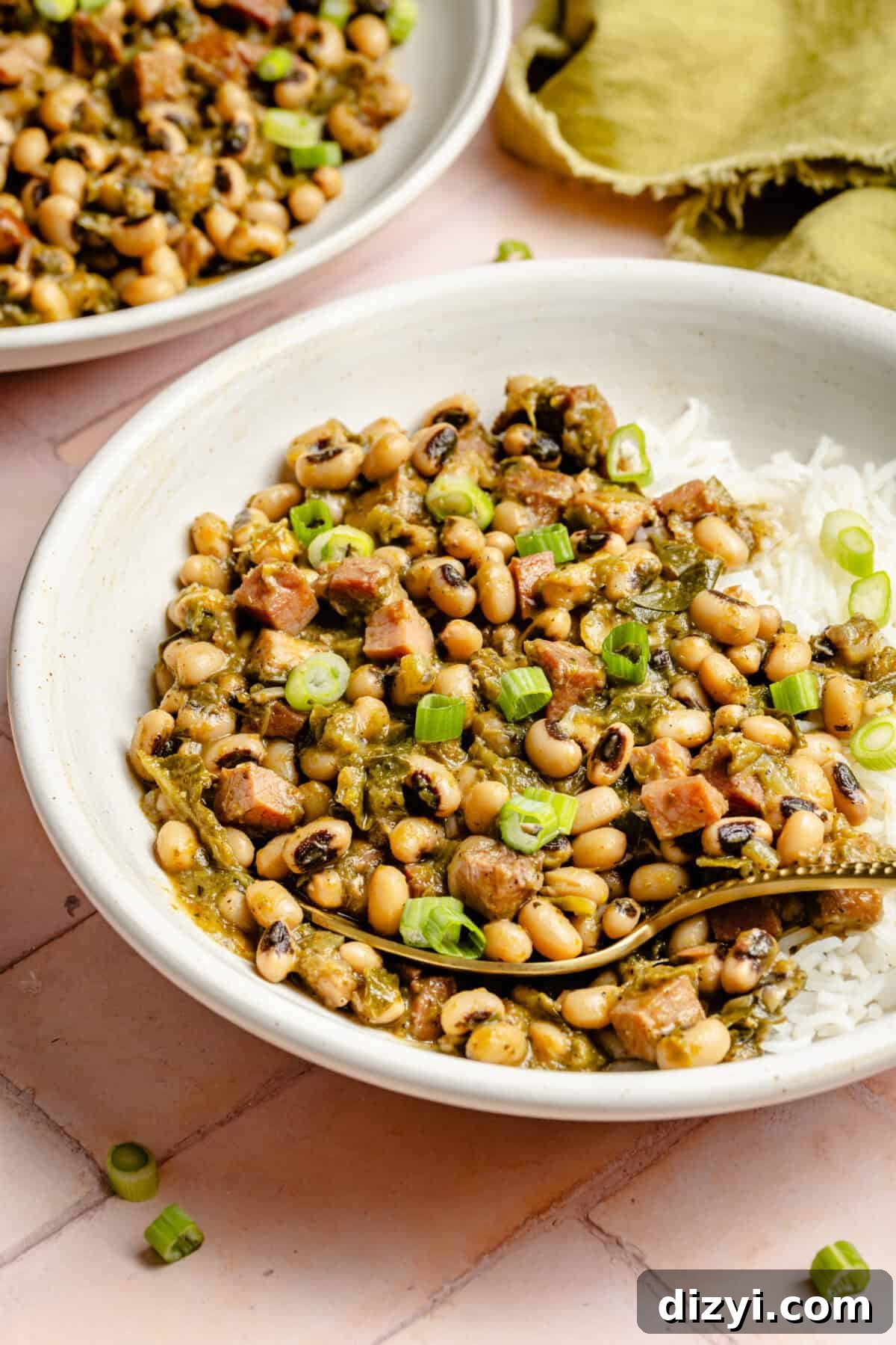 Classic Hoppin' John: Southern Black-Eyed Peas Recipe 3 Two completed dishes of Hoppin' Johns, served over white rice in white bowls. A green napkin is also on the counter.