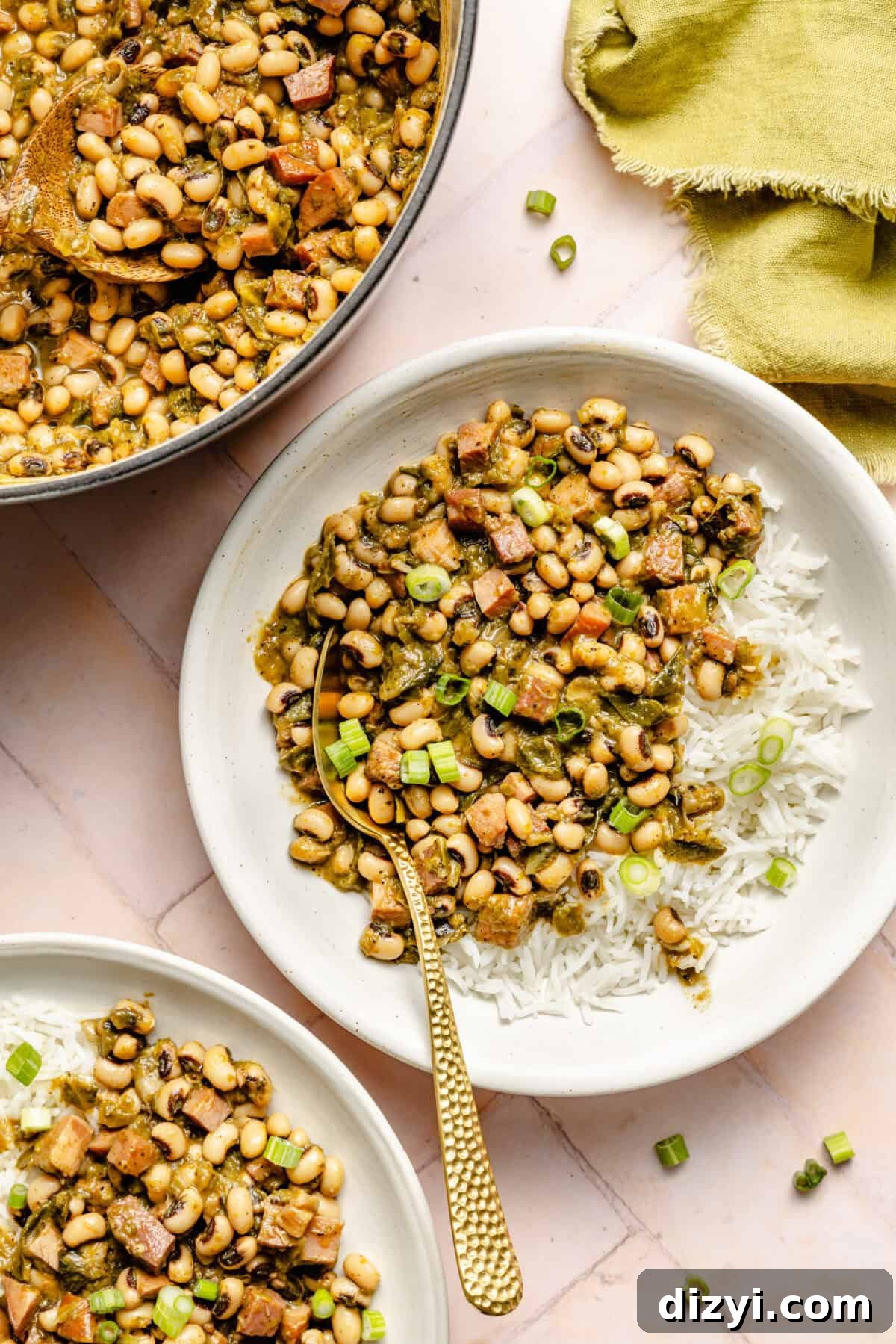 Classic Hoppin' John: Southern Black-Eyed Peas Recipe 5 A top-down view of two completed dishes of Hoppin' Johns, served over white rice in white bowls. A green napkin is also on the counter. The serving bowl of Hoppin' Johns is also visible in the image.