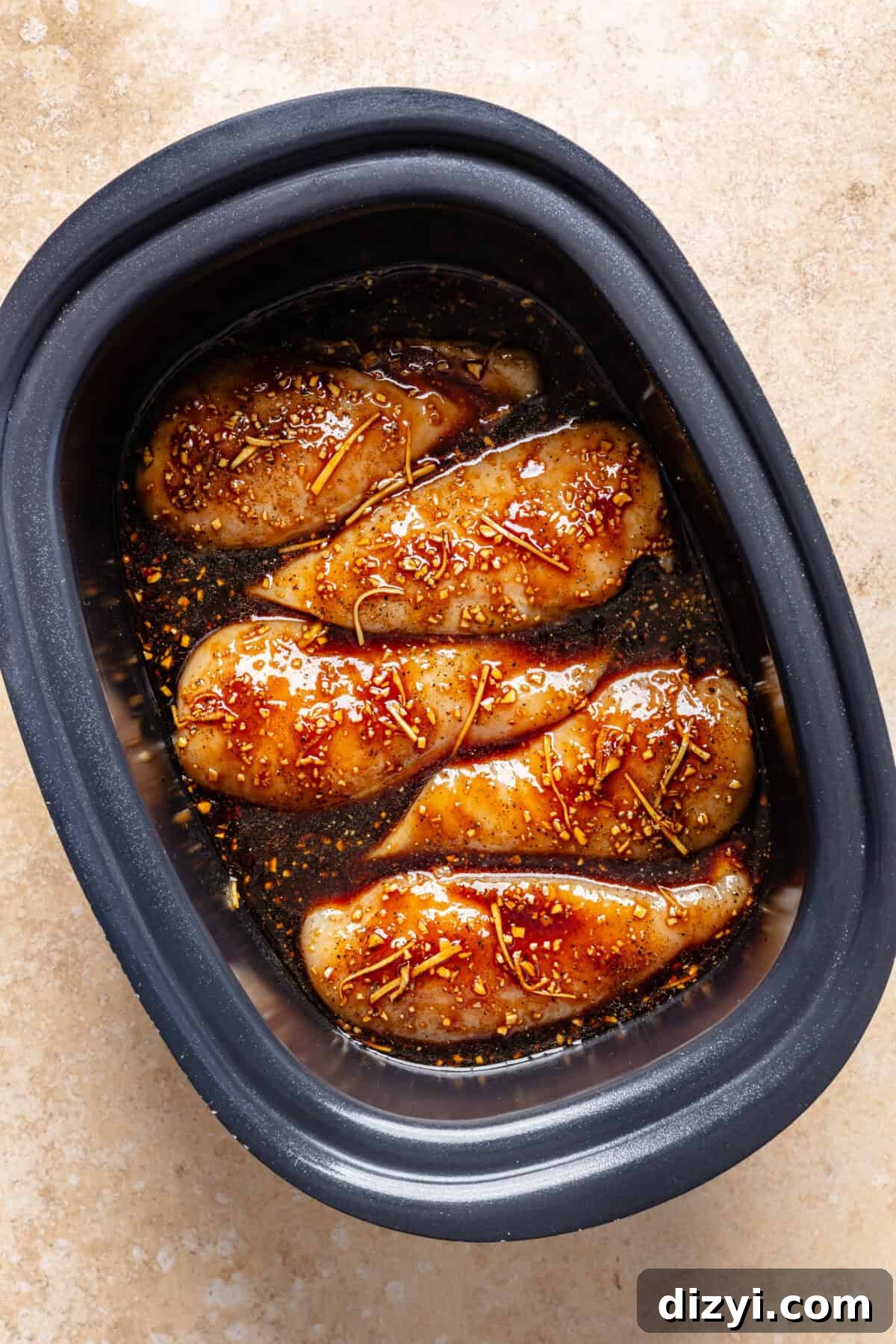 Raw chicken breasts nestled in slow cooker with sauce before it is cooked.