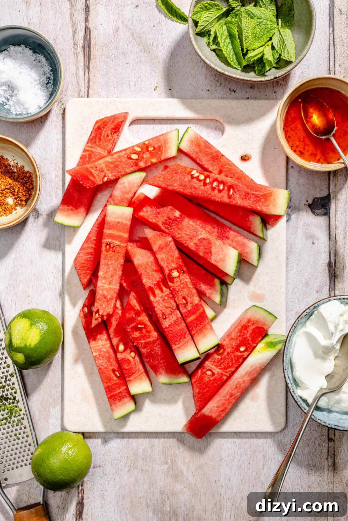 Chili-Lime Watermelon Salad with Labneh and Hot Honey Recipe 5 Sliced watermelon on cutting board with other ingredients scatter around.