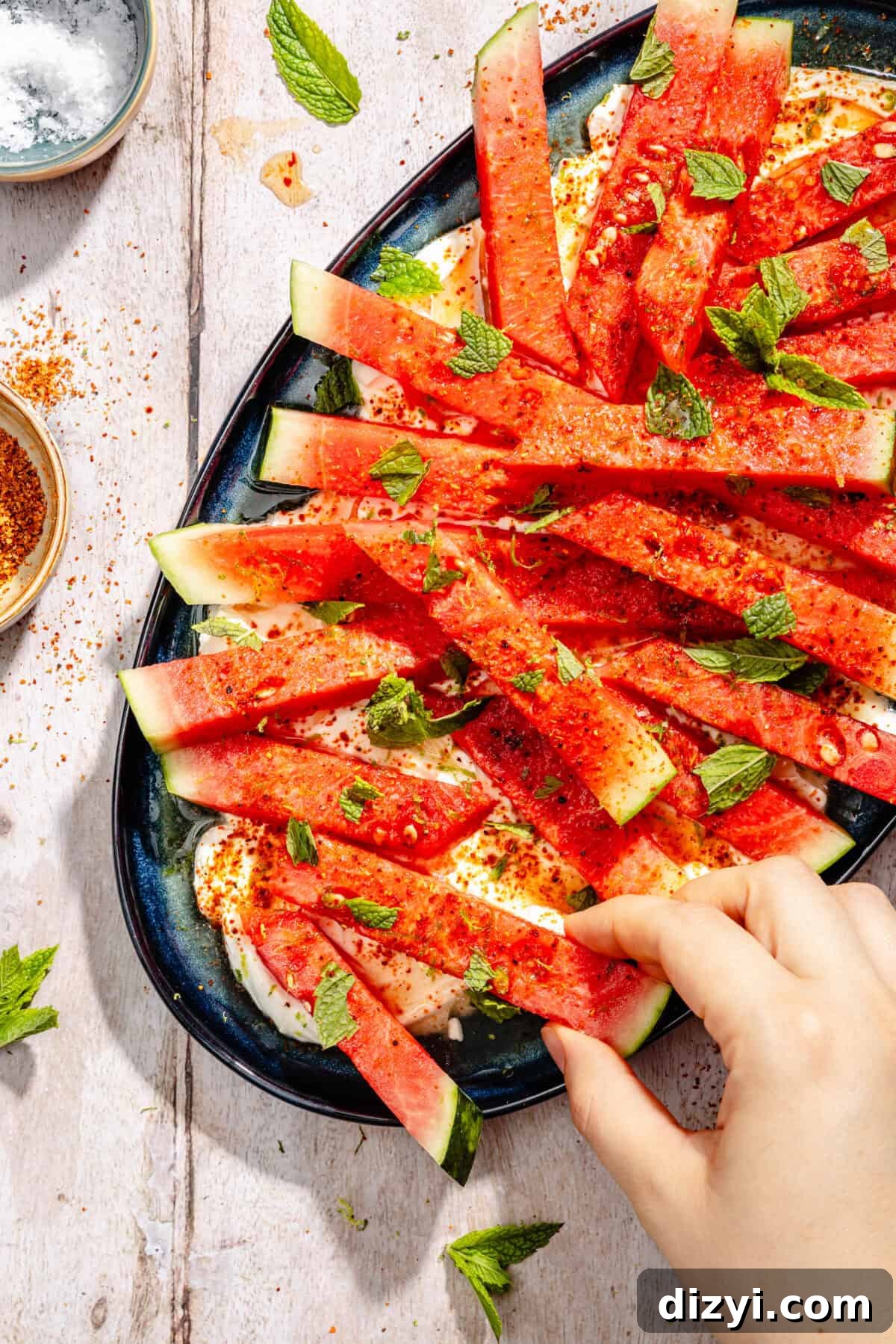 Chili-Lime Watermelon Salad with Labneh and Hot Honey Recipe 7 Hand grabbing slice of watermelon off of platter.